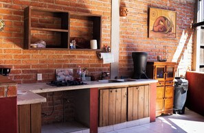 A kitchen with a brick wall, wooden cabinets, a sink, and a trash can.
