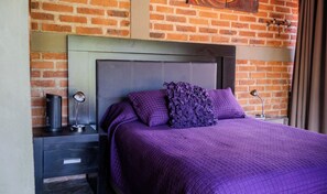 A bed with a headboard, a nightstand with a lamp, and a brick wall.