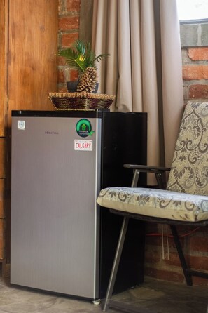 A compact Hisense refrigerator with a Calgary sticker, a wicker basket with a pine cone and a small plant, and a patterned chair.