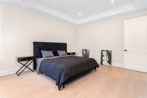 Een slaapkamer met een bed, nachtkastjes, een deur en twee foto's in lijsten aan de muur.