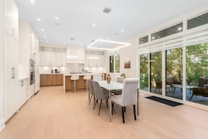 Een moderne keuken met witte kasten, een eethoek met een tafel en stoelen, en grote schuifdeuren naar een terras.