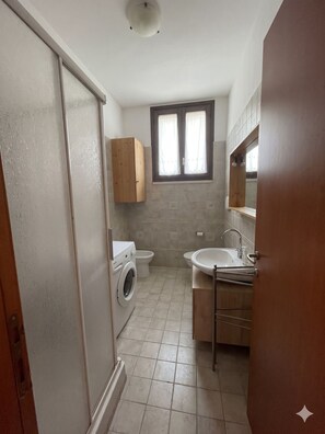 A compact bathroom with a washing machine, toilet, and sink.