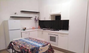 A compact kitchen with white cabinets, a gas stove, a built-in oven, and a refrigerator.