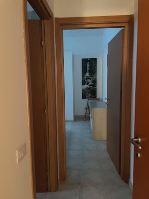 Un couloir avec un cadre de porte en bois, un sol carrelé et un tableau représentant une cascade accroché au mur.