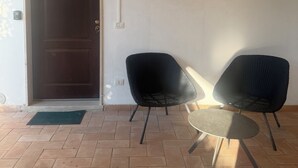 Ein Zimmer mit einer dunklen Holztür, zwei schwarzen Stühlen, einem kleinen runden Tisch und einer Wandleuchte.