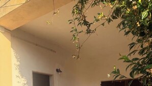 Ein überdachter Patio-Bereich mit einer Tür, zwei Stühlen und einem Fenster mit Rollläden.