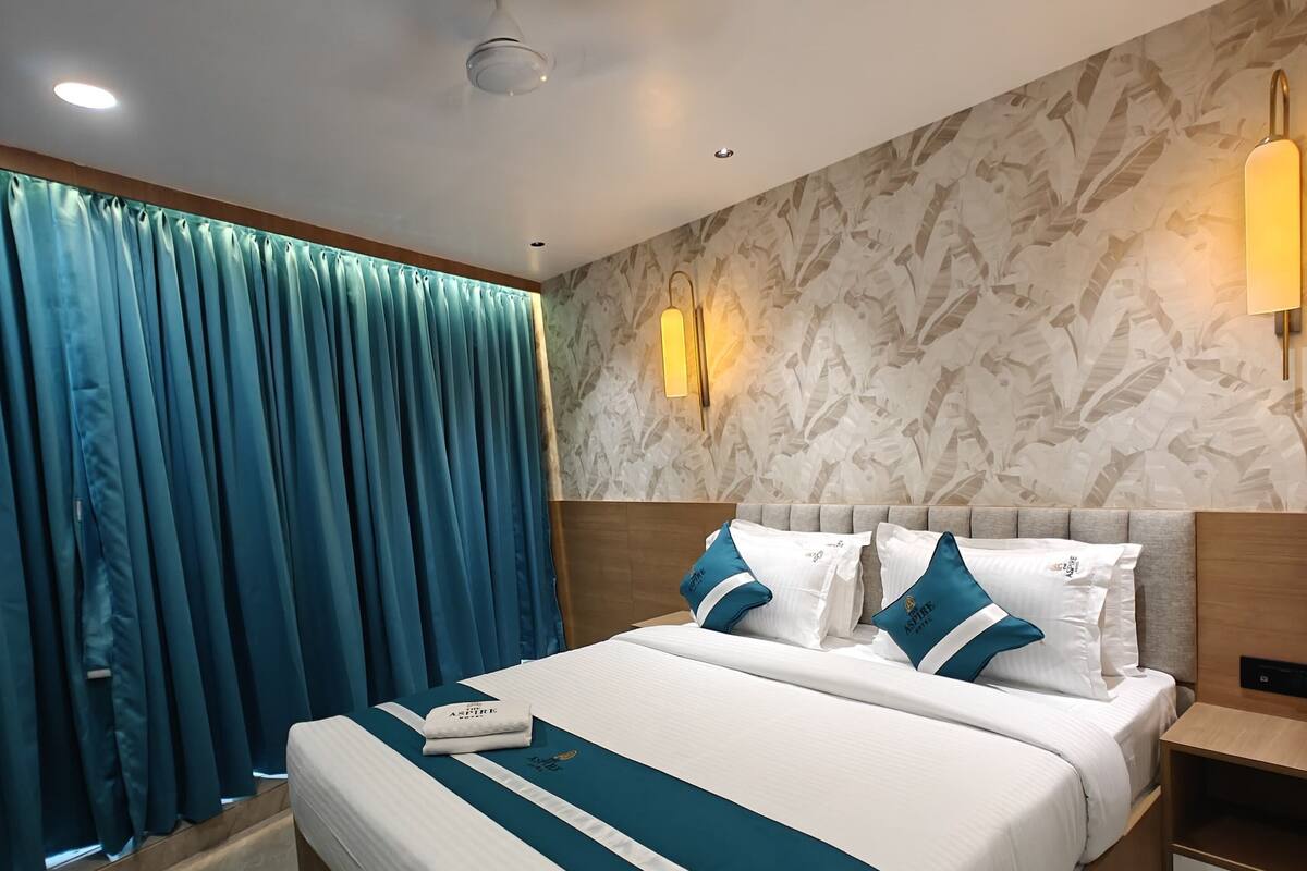 Ein modernes Hotelzimmer mit einem großen Bett, einem Nachttisch, einer Wandlampe und einem Fenster mit Vorhängen.