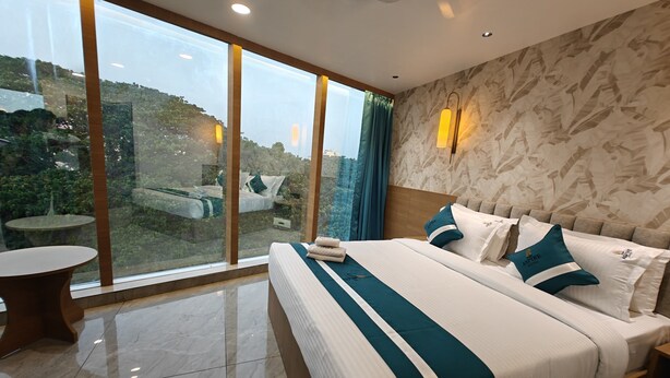 A hotel room with a large bed, a round table, and a view of greenery through floor-to-ceiling windows. - The Aspire Hotel Guwahati (Guwahati)