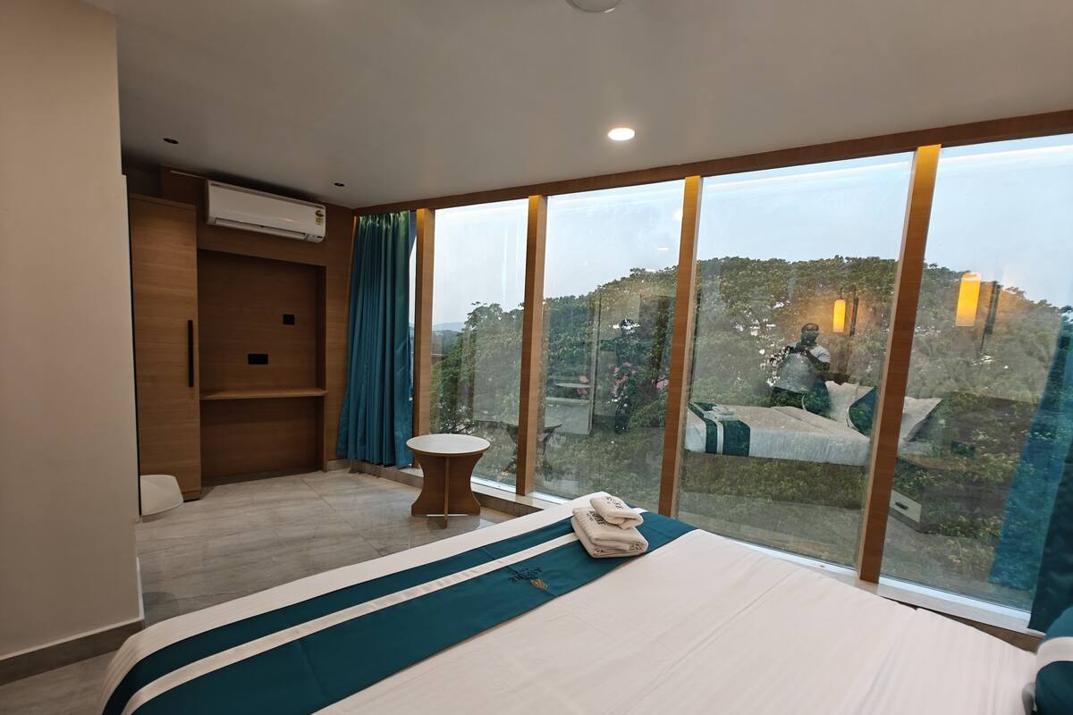 Ein Hotelzimmer mit einem großen Bett, einem kleinen runden Tisch, einem Einbauschrank und einem großen Fenster mit Blick ins Freie.