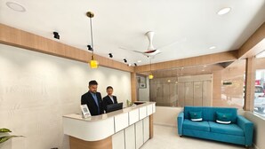 A reception area with a reception desk, two staff members, a blue sofa, and a ceiling fan. - The Aspire Hotel Guwahati (Guwahati)