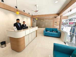 A reception area with a counter, two staff members, a blue sofa, and a ceiling fan. - The Aspire Hotel Guwahati (Guwahati)
