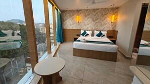 A hotel room with a large bed, a small round table, a balcony with a view, and a ceiling fan. - The Aspire Hotel Guwahati (Guwahati)