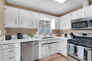Una cocina moderna con armarios blancos, lavavajillas de acero inoxidable, microondas y estufa a gas.