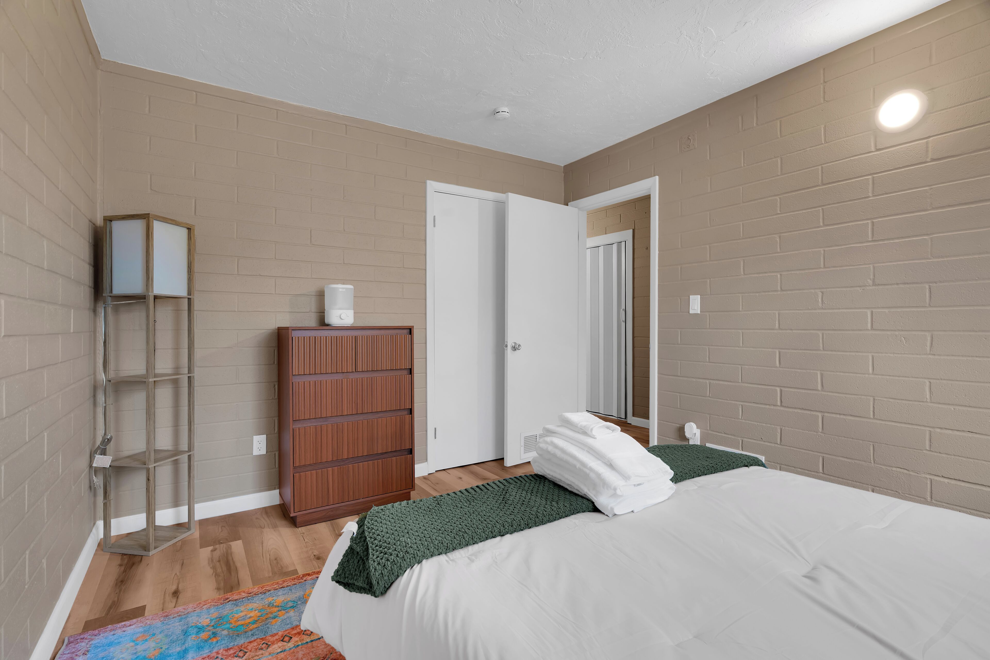 A bedroom with a bed, a dresser, a wardrobe, a mirror, and a shelf.