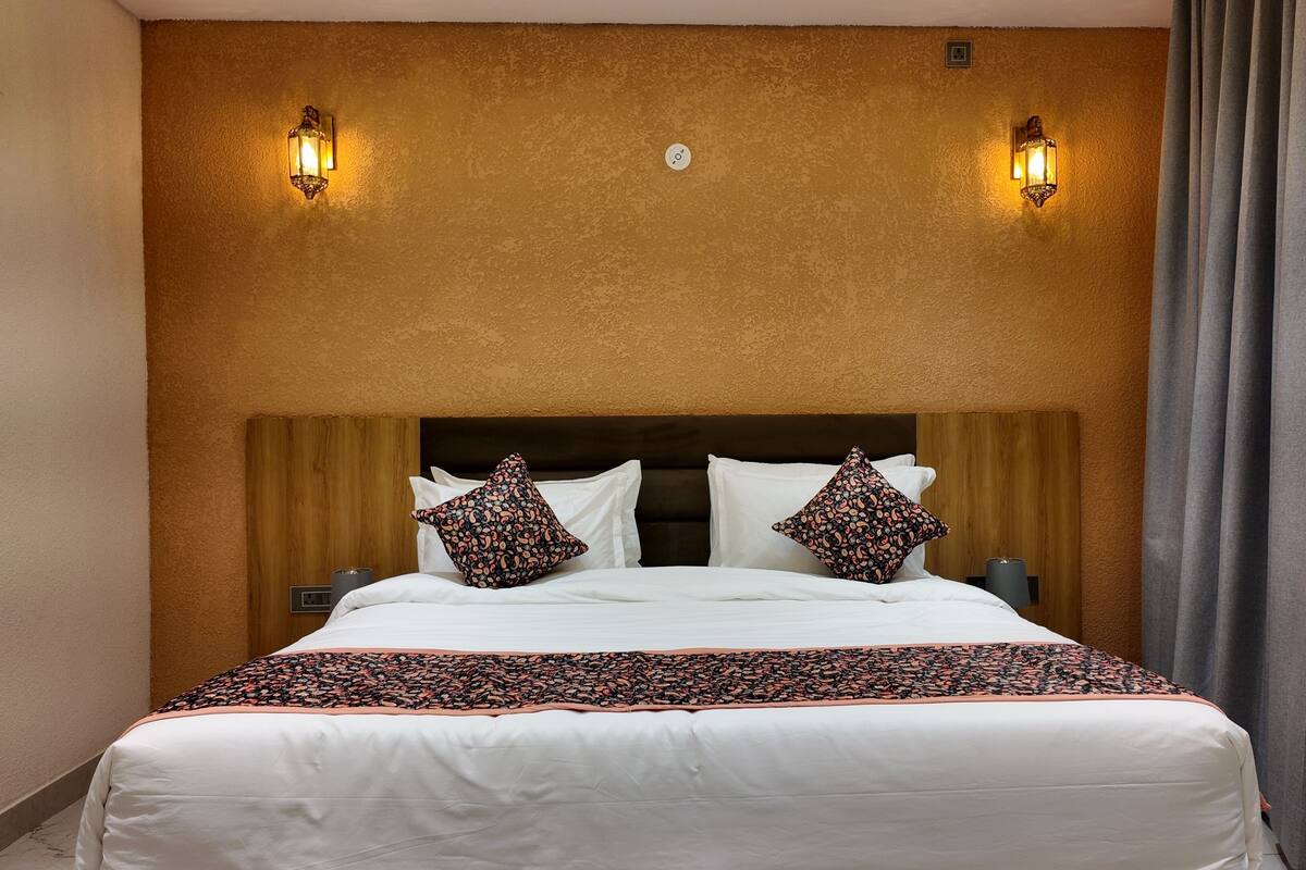 Una habitación de hotel con una cama grande, dos apliques, un cabecero de madera y una manta decorativa.