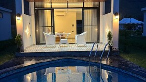 Zona de piscina exterior moderna con vista despejada, área de descanso cubierta con sillas y entrada bien iluminada.