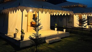 Una carpa grande y bien iluminada con techo plano, rodeada de césped y algunas plantas en macetas.
