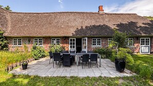 A brick house with a thatched roof, a patio with a table and chairs, and a garden. - 6 bedroom gorgeous home in Ribe (Ribe)