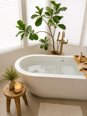 Een moderne badkamer met een vrijstaand bad, een potplant, een kaars en een houten dienblad met toiletartikelen.