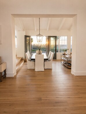 A dining area with a wooden table and chairs, a hanging light fixture, and a view through a glass door. - Ocean View Retreat, Private Pool, Minutes to the Beach & Downtown Encinitas (Encinitas)