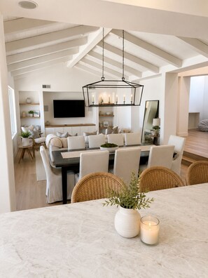 Een moderne eetruimte met een marmeren tafel, rieten stoelen en een kroonluchter.