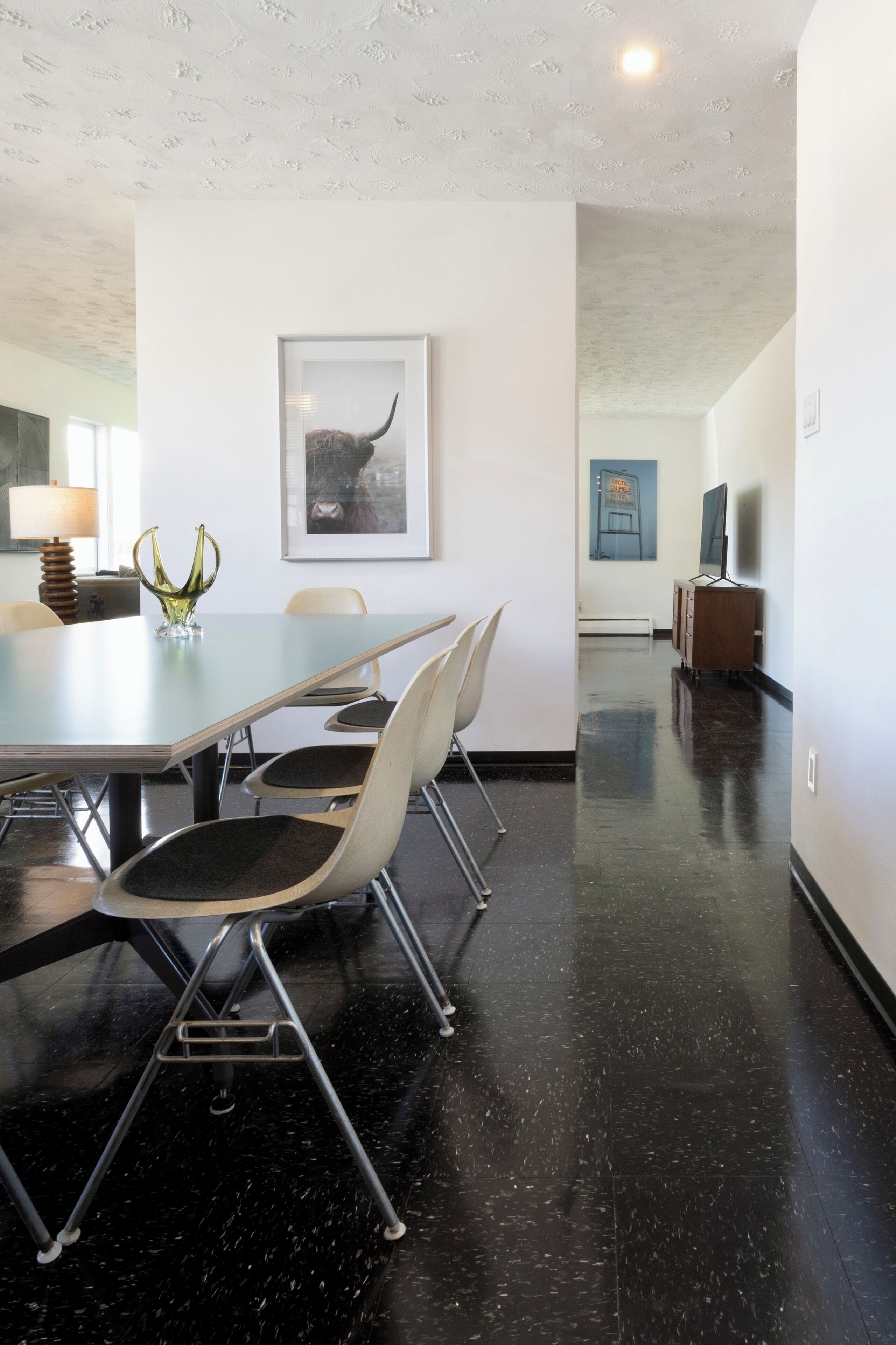 A conference room with a long table, four chairs, a vase, and a framed picture on the wall.
