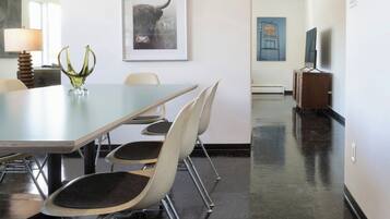 A conference room with a long table, four chairs, a vase, and a framed picture on the wall.