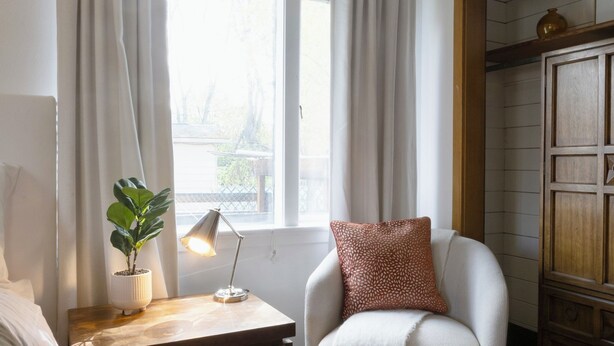 A room with a bed, a chair, a nightstand with a lamp, a plant, and a window with curtains. - Serene 2-bedroom bed & breakfast in Anchorage welcomes you (Anchorage)