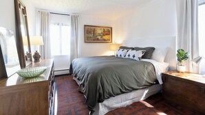 A bedroom with a bed, a bedside table with a lamp, a mirror, a painting on the wall, and a window with curtains. - Serene 2-bedroom bed & breakfast in Anchorage welcomes you (Anchorage)