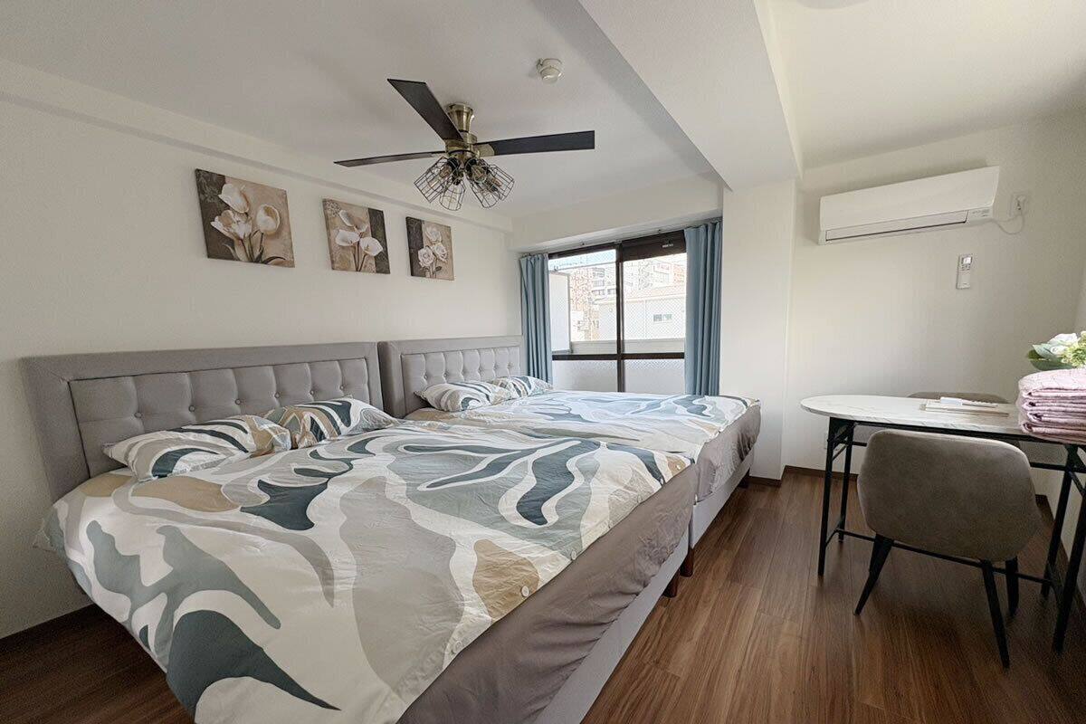 Un dormitorio con cama, escritorio, silla, ventilador de techo y obras de arte en la pared.