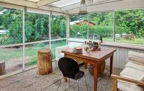 Une véranda avec une table, des chaises et une vue sur le jardin.