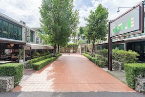 A paved walkway flanked by neatly trimmed hedges and modern buildings with large windows.