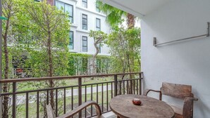 Ein Balkon mit Holztisch und -stühlen, einem Metallgeländer und Blick auf ein Gebäude und Grünflächen.