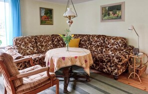 Ett rum med en soffa med blommönster, en trästol, ett litet runt bord med en duk med blommönster och två tavlor som hänger på väggen.