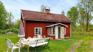 Una casa de madera roja con una puerta blanca, un porche pequeño y una mesa de picnic con sillas.