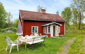Ett rött trähus med en vit dörr, en liten veranda och ett picknickbord med stolar.