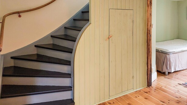 Una escalera con peldaños negros que conduce a una habitación con una cama y piso de madera.