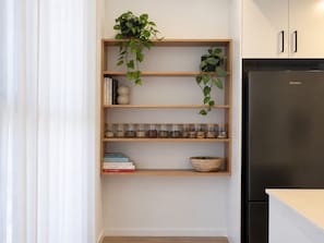 A kitchen with a built-in wooden shelf unit, a black refrigerator, and a potted plant. - Moonee Ponds Luxe by Ready Set Stay (Moonee Ponds)