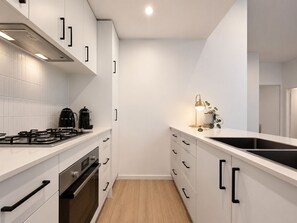 Una cocina moderna con armarios blancos, estufa a gas, cafetera y una pequeña planta en la encimera.