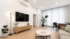 Uma sala de estar moderna com televisão de tela plana, console de madeira, mesa de centro redonda e um espaço de jantar com mesa e cadeiras.