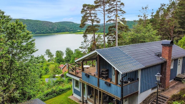 Eine zweistöckige Holzhütte mit einem Balkon mit Blick auf einen See, umgeben von Bäumen.