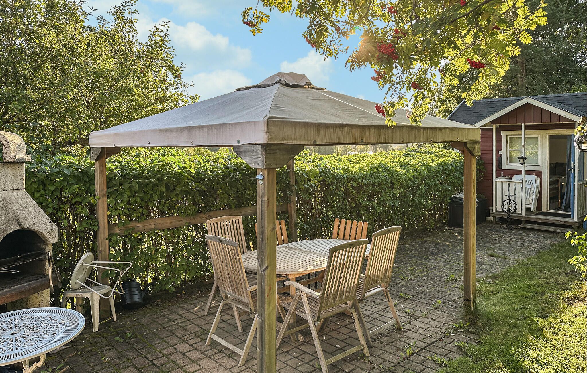 A covered outdoor patio with a table and chairs, a grill, and a small shed.