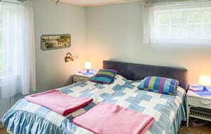 Ein Schlafzimmer mit Bett, Nachttischen, einer Lampe, einem Fenster mit Vorhängen und einem Wandbild.