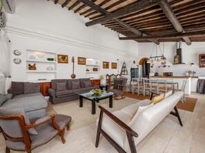 Ein Wohnzimmer mit einer Couch, Sesseln, einem Esstisch und einer Küchenzeile.