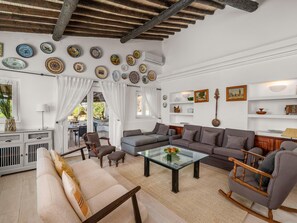 Ein Wohnzimmer mit einer Couch, Sesseln, einem Glastisch und einem Essbereich mit Tisch und Stühlen.