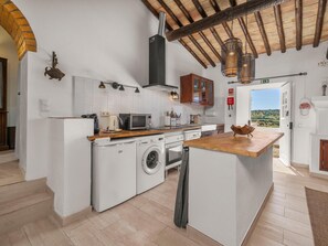 A compact kitchen with a washing machine, microwave, and wooden counter. - Quinta da Luz, Rustic Villa with Pool and Sea Views (Luz, Lagos)