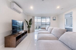 Una sala de estar moderna con un televisor de pantalla plana, un mueble de madera para entretenimiento, un sofá grande y una planta en maceta.