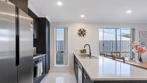 Una cocina moderna con un refrigerador de acero inoxidable, una isla central con un lavamanos y un comedor con sillas.