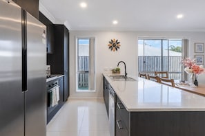 Una cocina moderna con un refrigerador de acero inoxidable, una isla central con un lavamanos y un comedor con sillas.