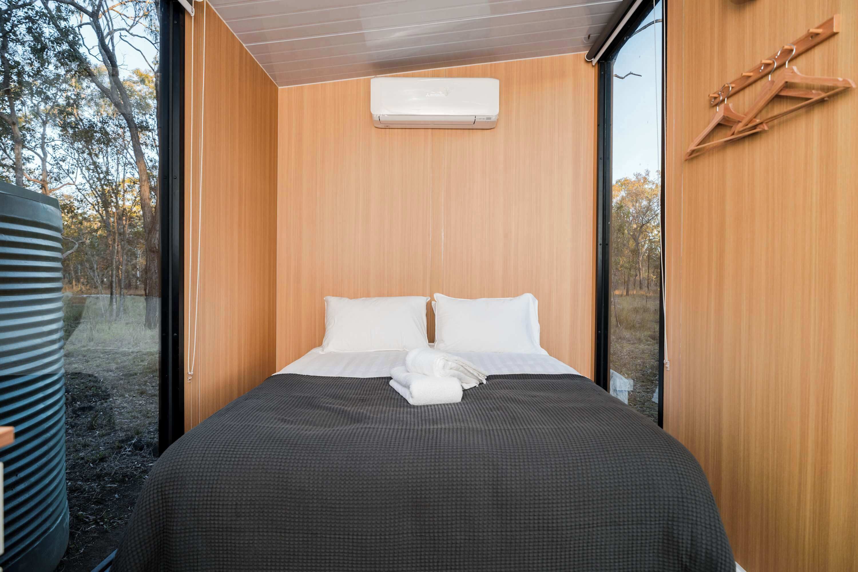 A modern bedroom with a large bed, wooden walls, and a view of trees through a window.